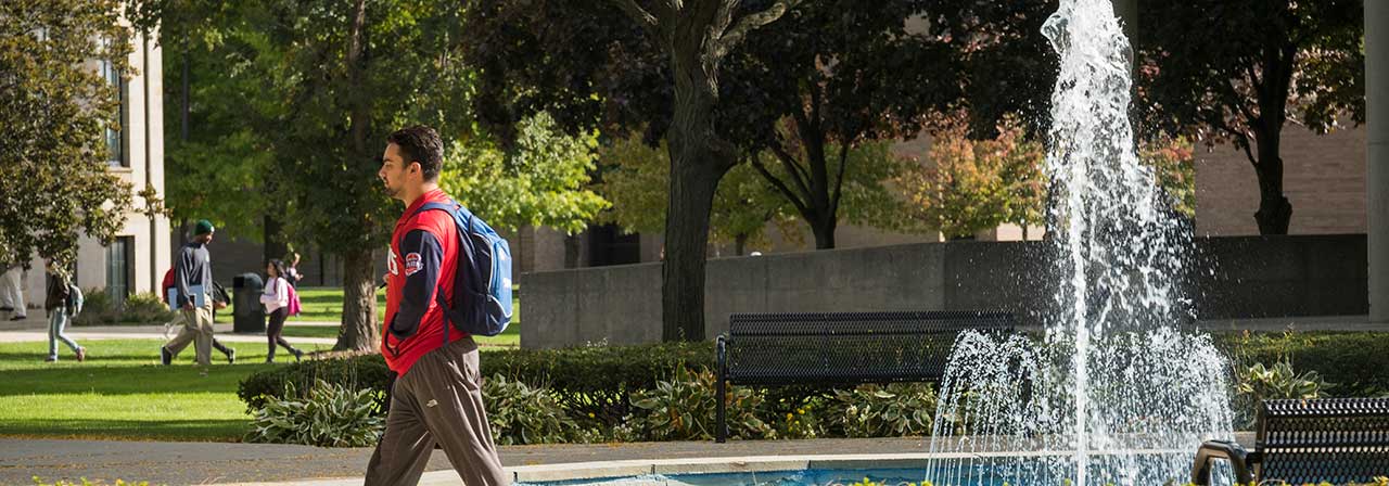 Male student walking near the McNichols Campus fountain