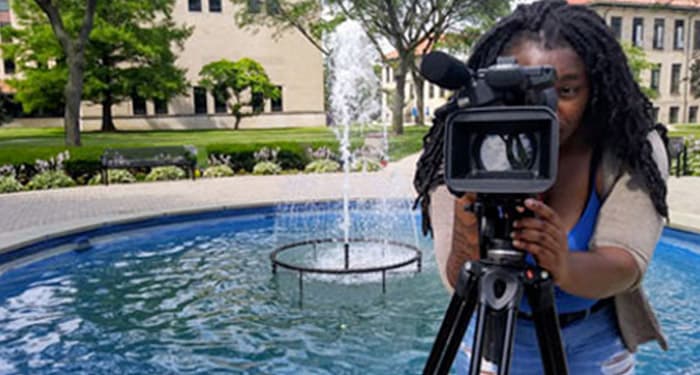 Female student with a camera in front of the fountain on McNichols Campus